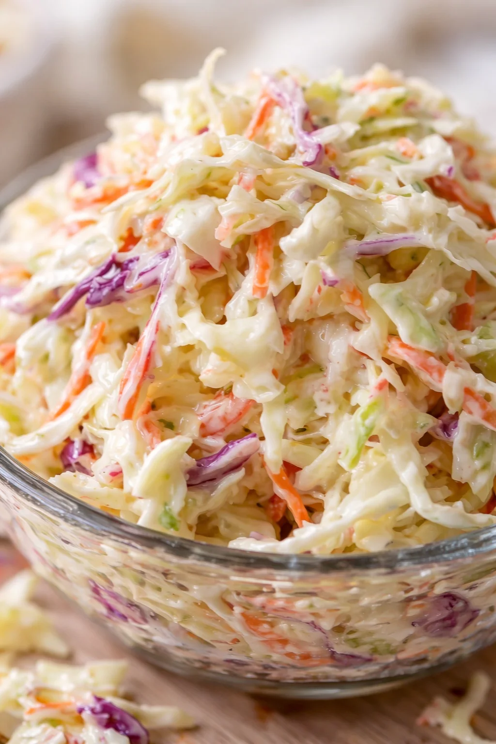 Creamy coleslaw piled high in a glass bowl with shredded cabbage, carrots, and purple cabbage.