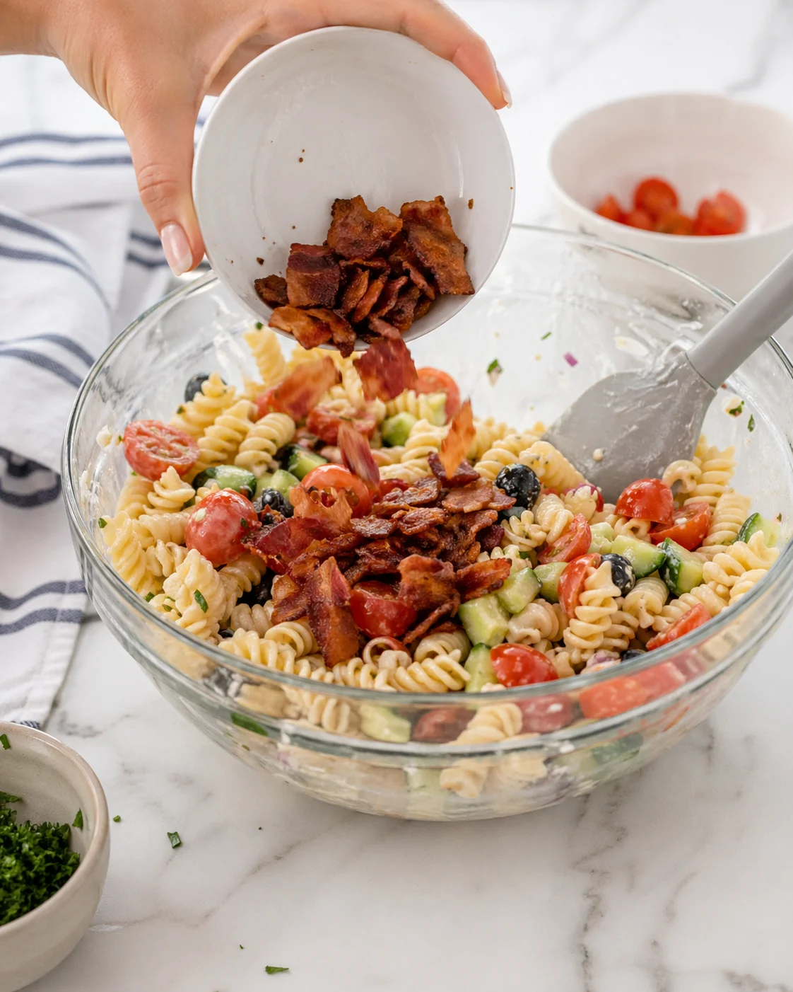 Crispy bacon crumbles being sprinkled over the finished pasta salad.