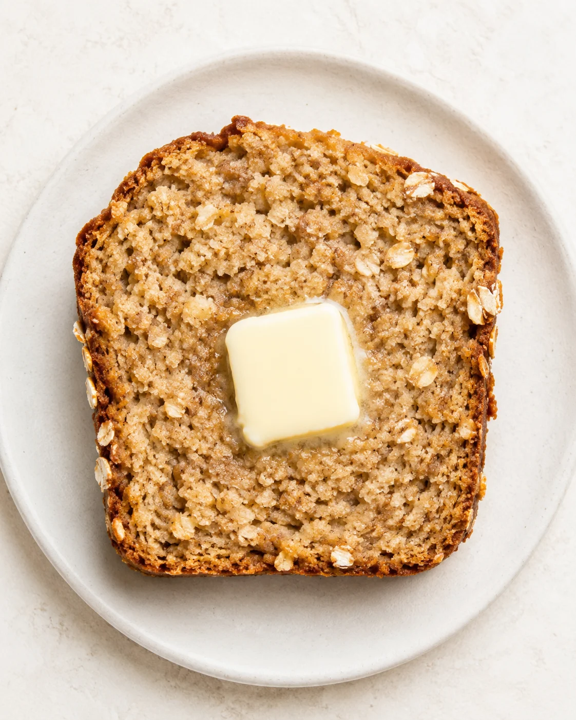 Top-down view of banana bread slice on a white plate with melting butter.