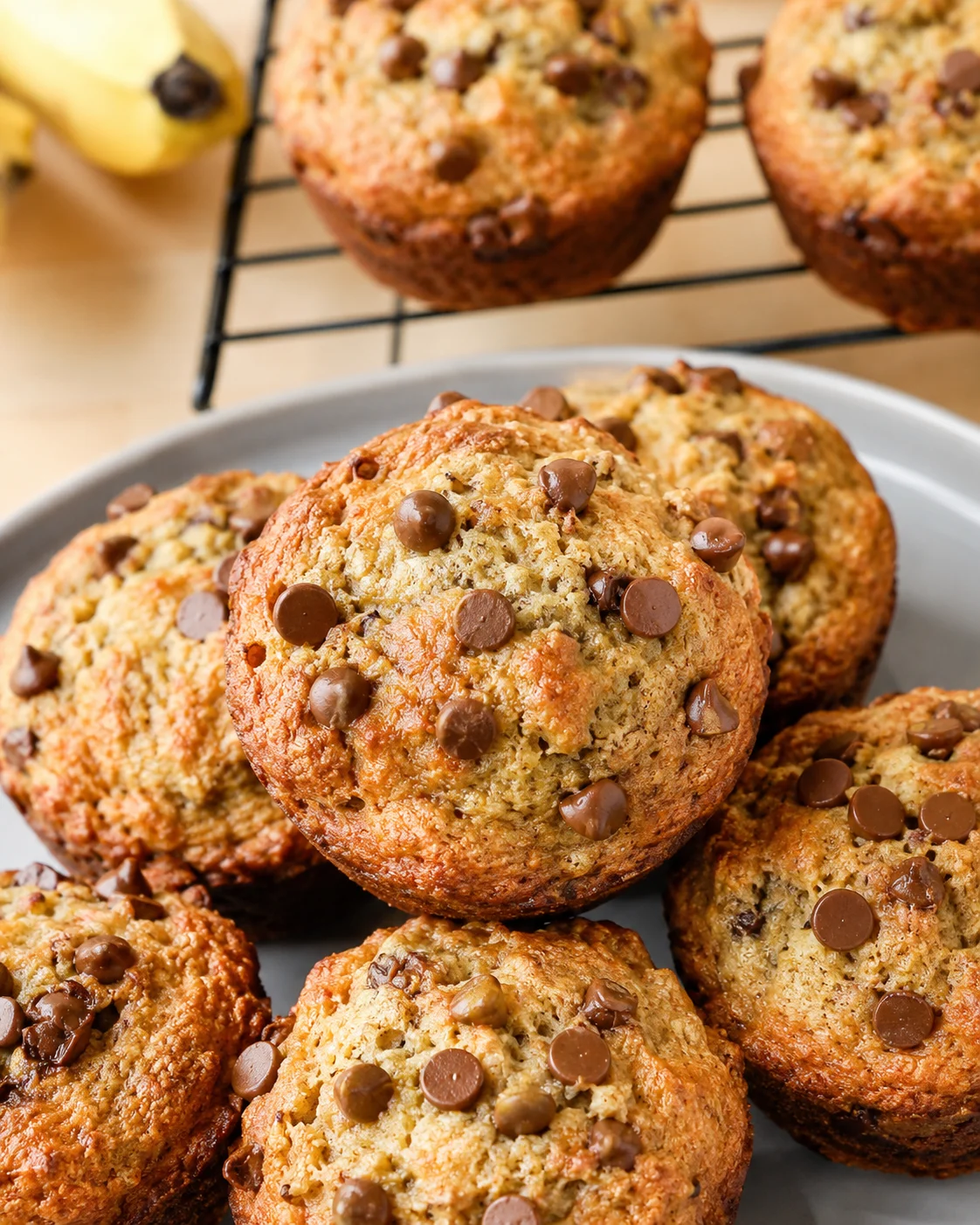 Close-up of golden-brown banana muffins studded with chocolate chips on a gray plate.