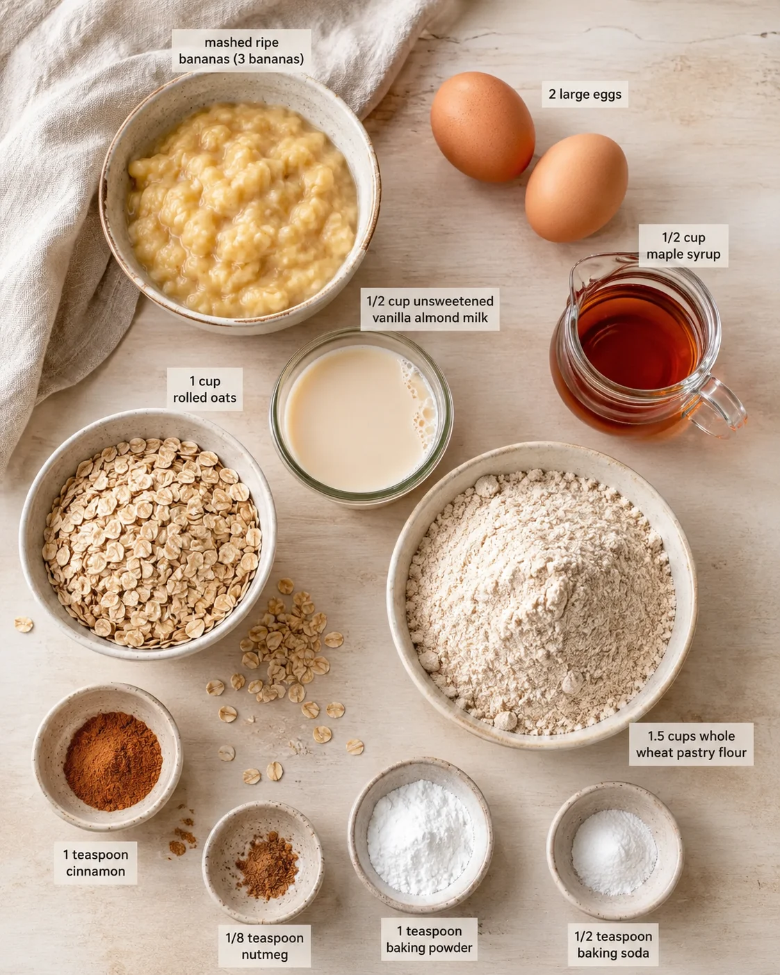Top-down view of baking ingredients: mashed bananas, eggs, maple syrup, almond milk, oats, flour, spices.