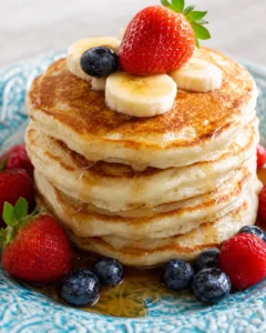 Stack of fluffy pancakes topped with banana slices and a strawberry on a blue patterned plate.