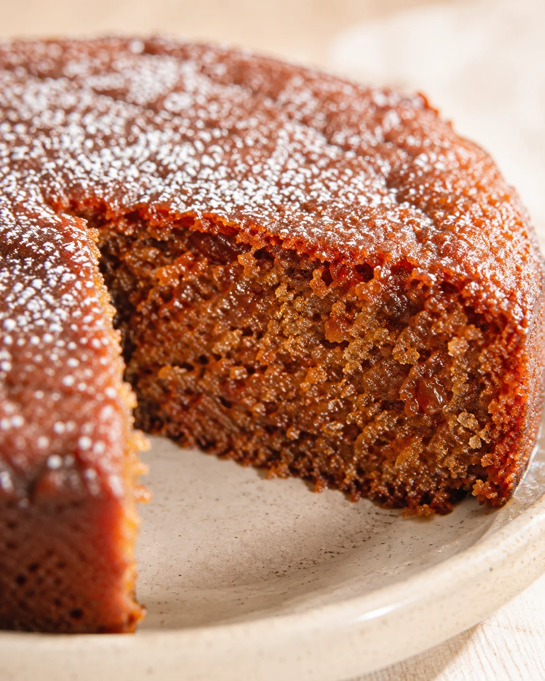 dense brown sugar cake slice with sugar crystals on top on a beige plate