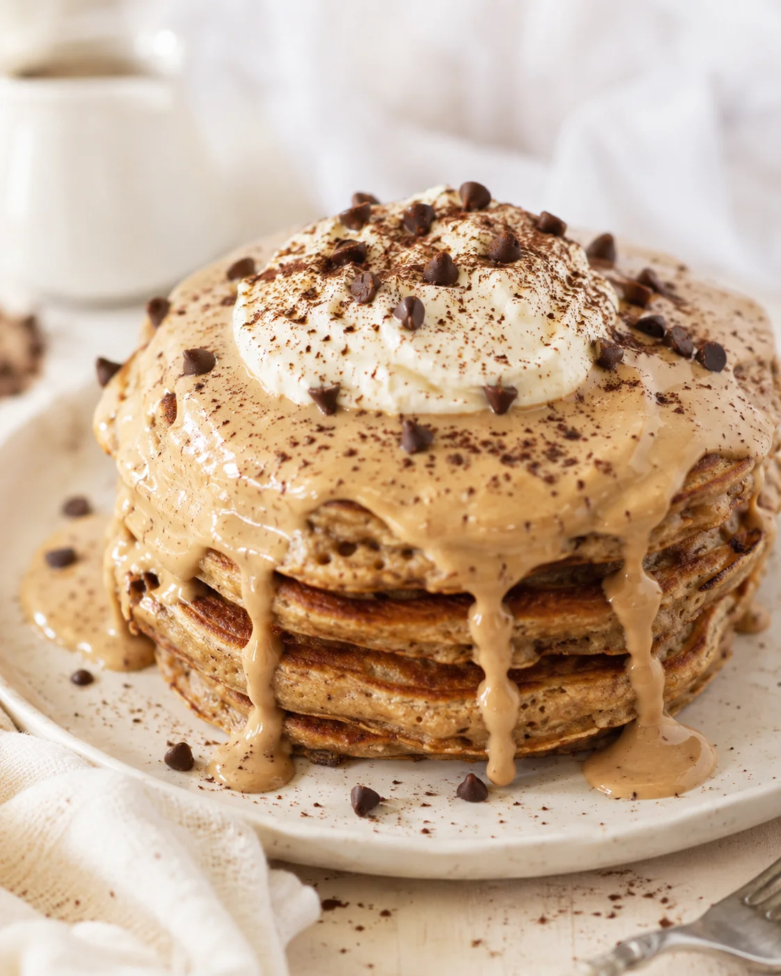 Stack of pancakes with caramel sauce, whipped cream, and scattered chocolate chips.