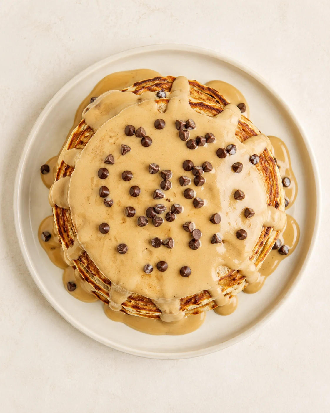 top-down view of a tall caramel-drizzled pancake stack with chocolate chips on a beige plate