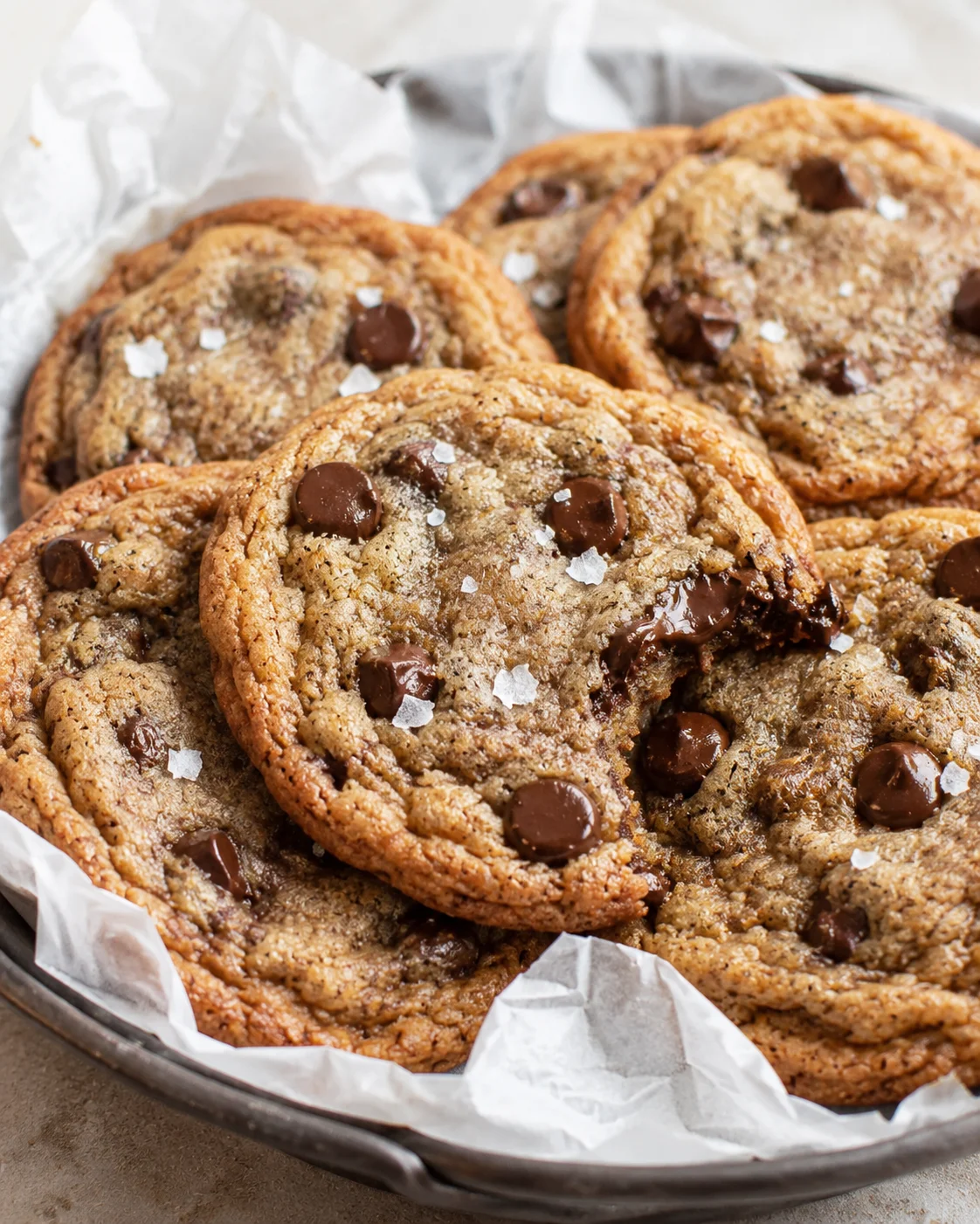 golden-brown chocolate chip cookies on parchment-lined baking sheet with flaky sea salt.