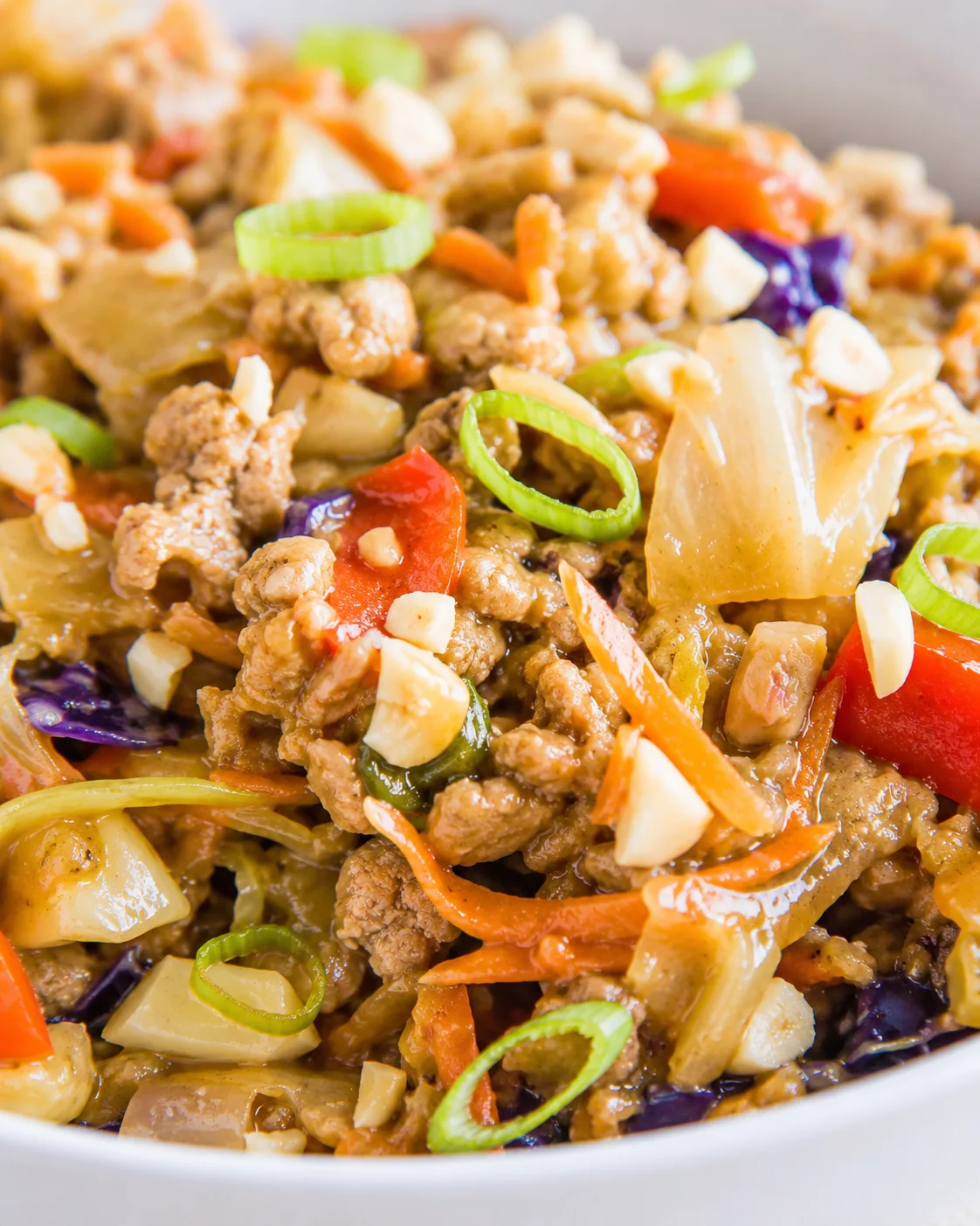 close-up of colorful chicken stir-fry with carrots, peppers, onions, cabbage, and green onion rings.