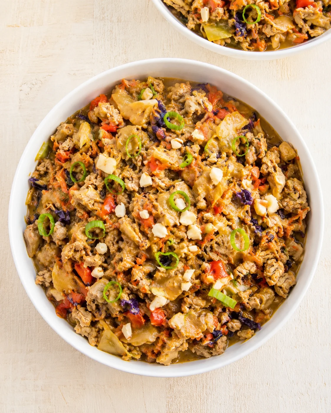 white bowl filled with colorful ground-meat mixture, diced red peppers, cabbage, cheese, and green onion rings