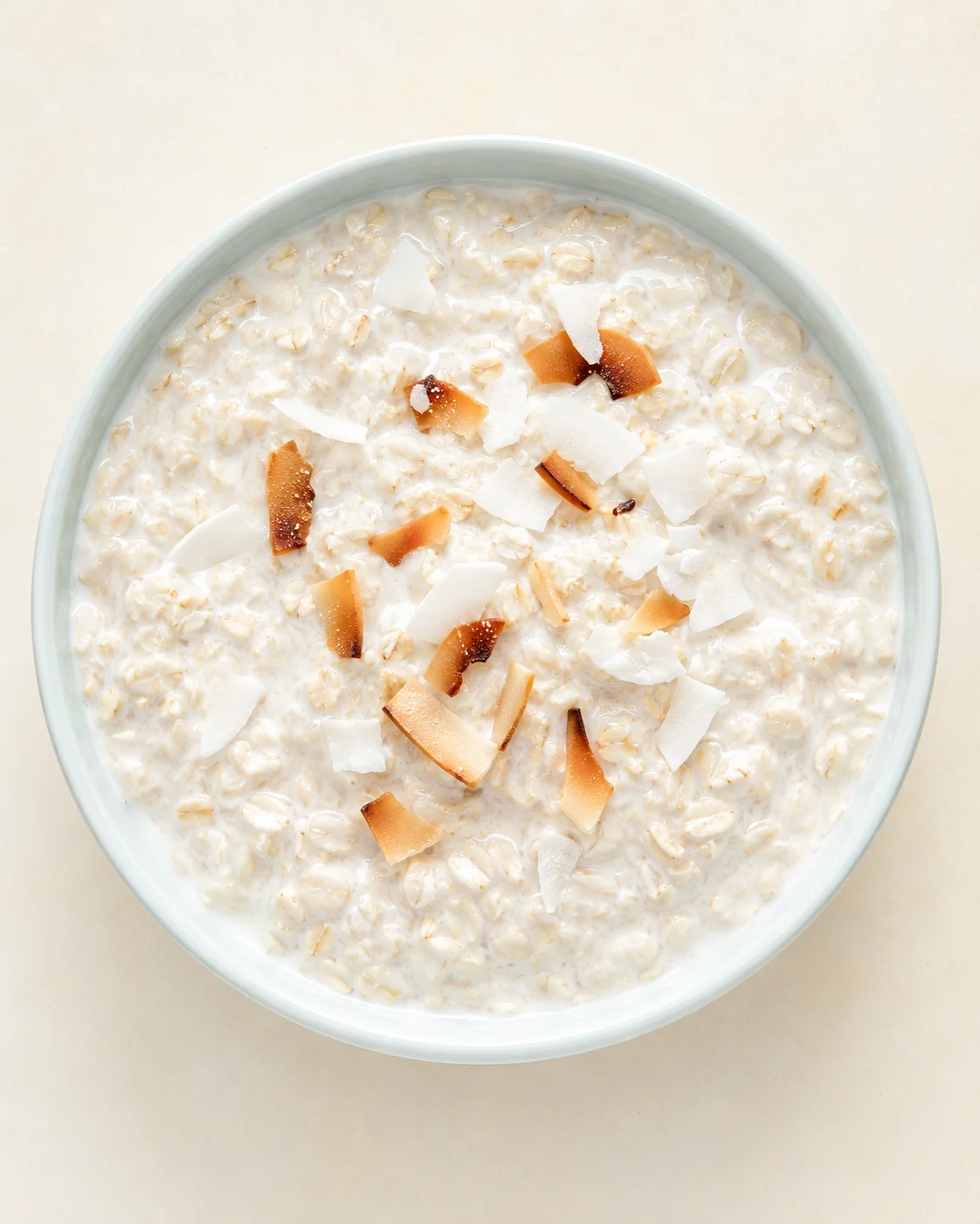 top-down view of a pale blue bowl filled with creamy oatmeal, topped with coconut flakes