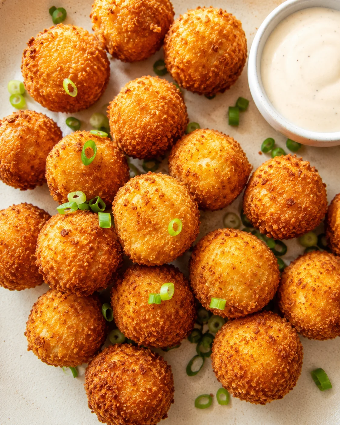golden-brown breadcrumb-coated cheese balls arranged on a beige plate with a creamy dipping sauce.