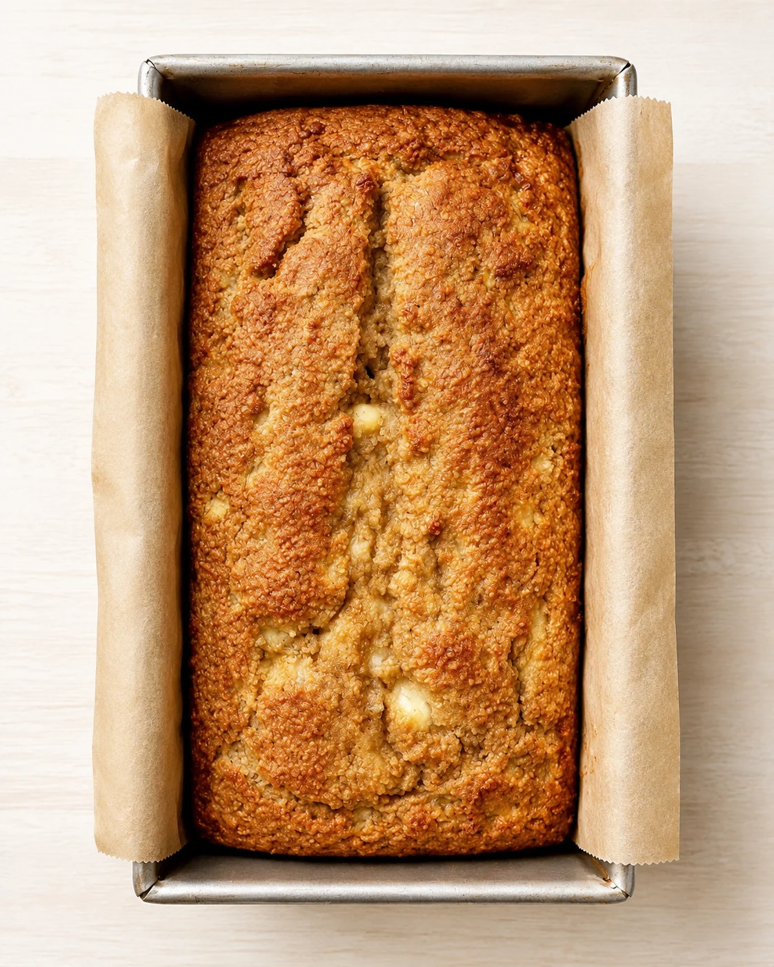 top-down view of a golden-brown loaf of bread in a parchment-lined loaf pan.