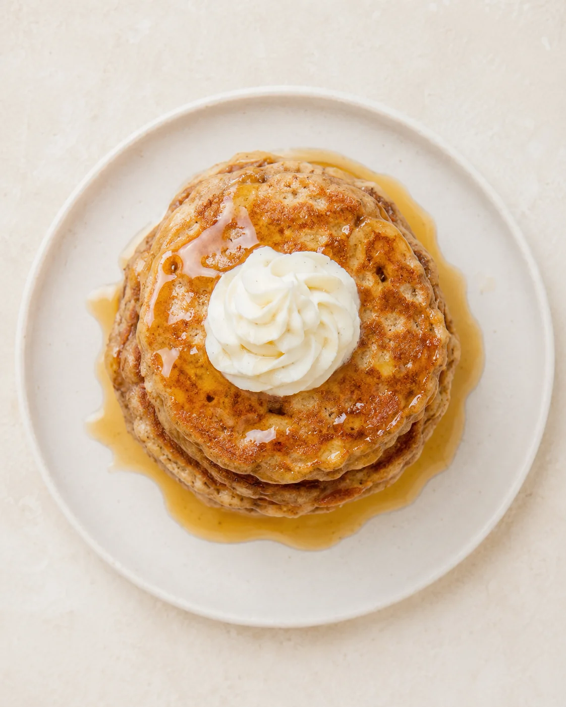 stack of golden pancakes with whipped cream and amber syrup on a white plate.