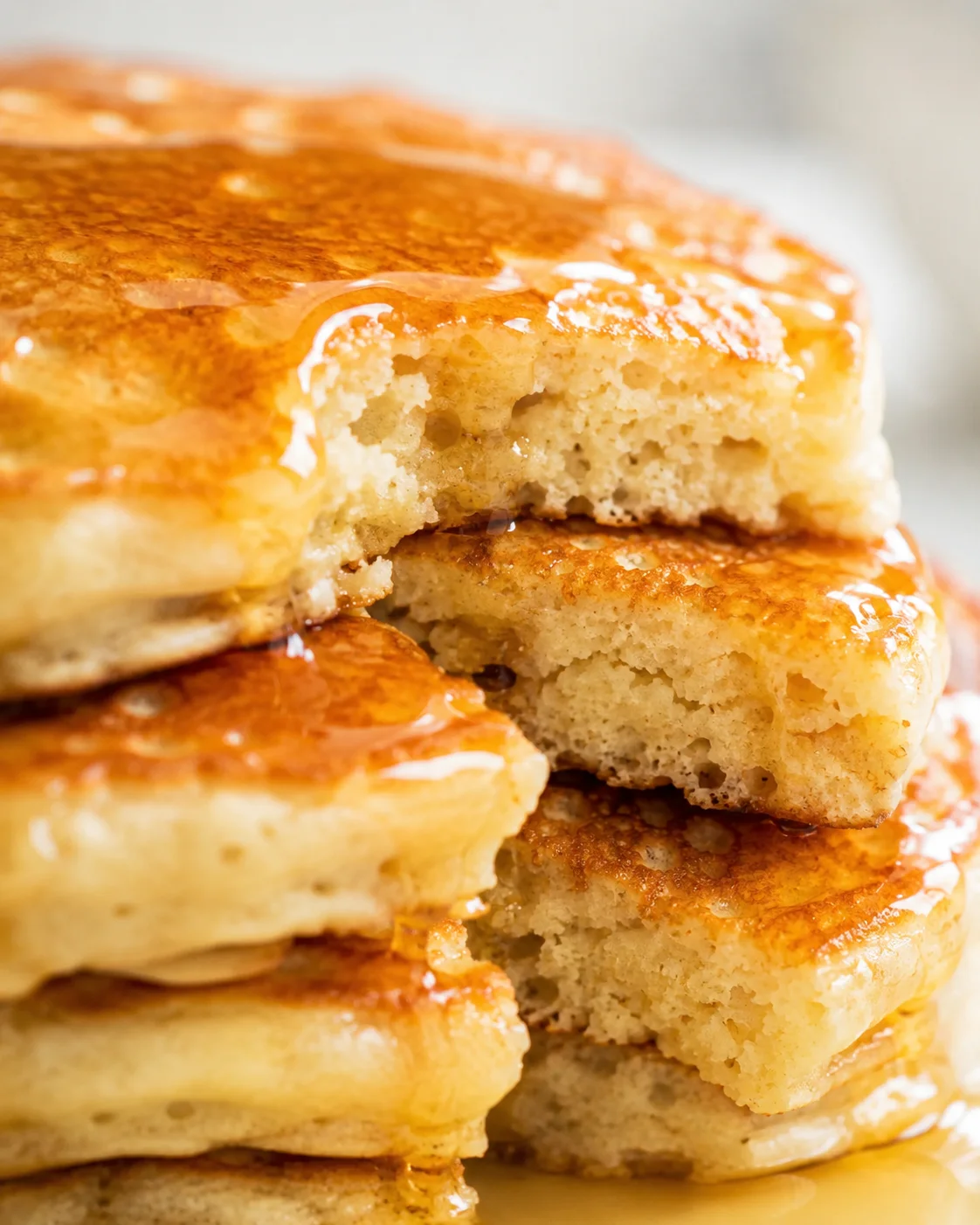close-up of a tall stack of fluffy pancakes with syrup dripping over the sides