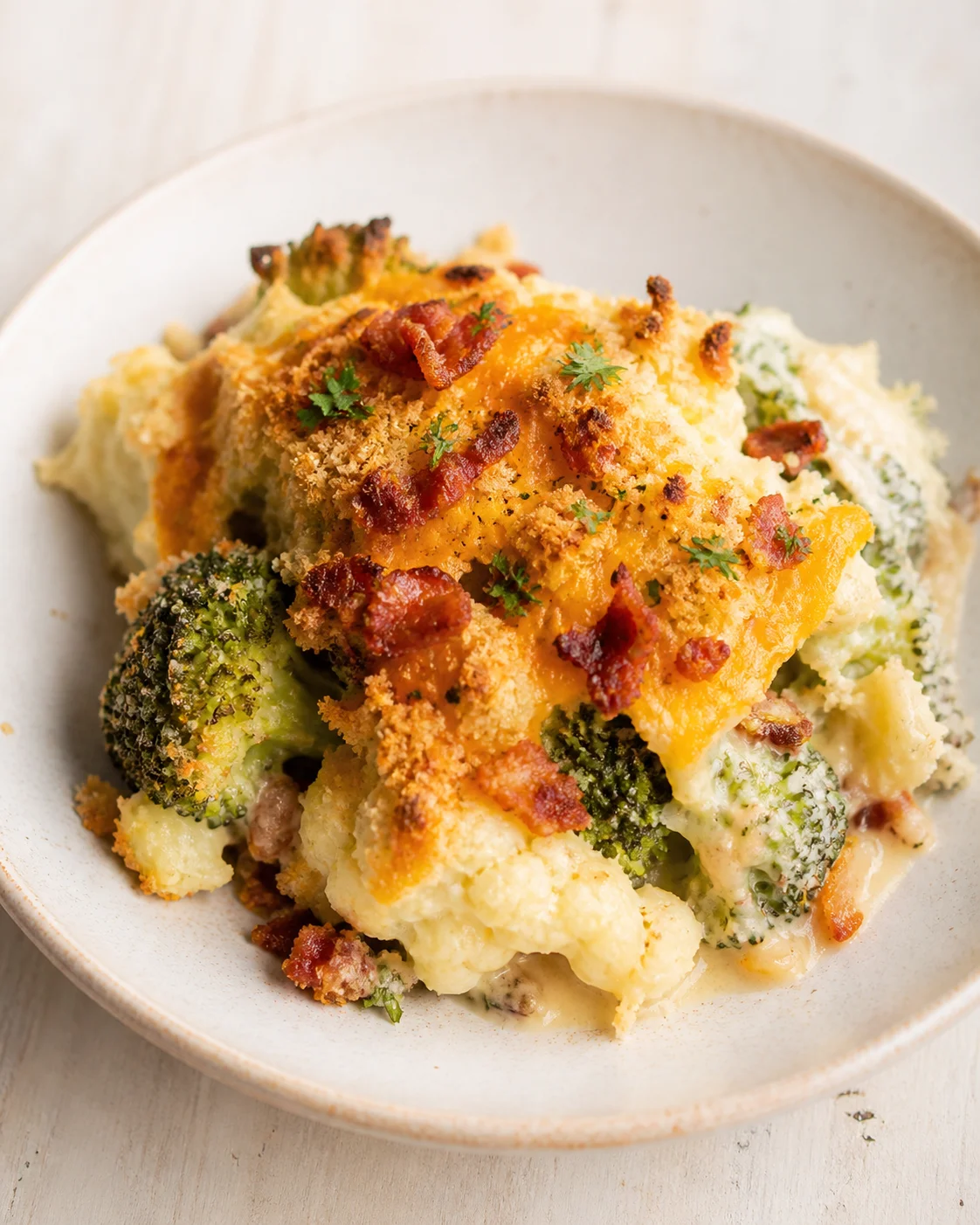 Broccoli and cauliflower bake with cheddar, bacon, and breadcrumbs on a beige plate.