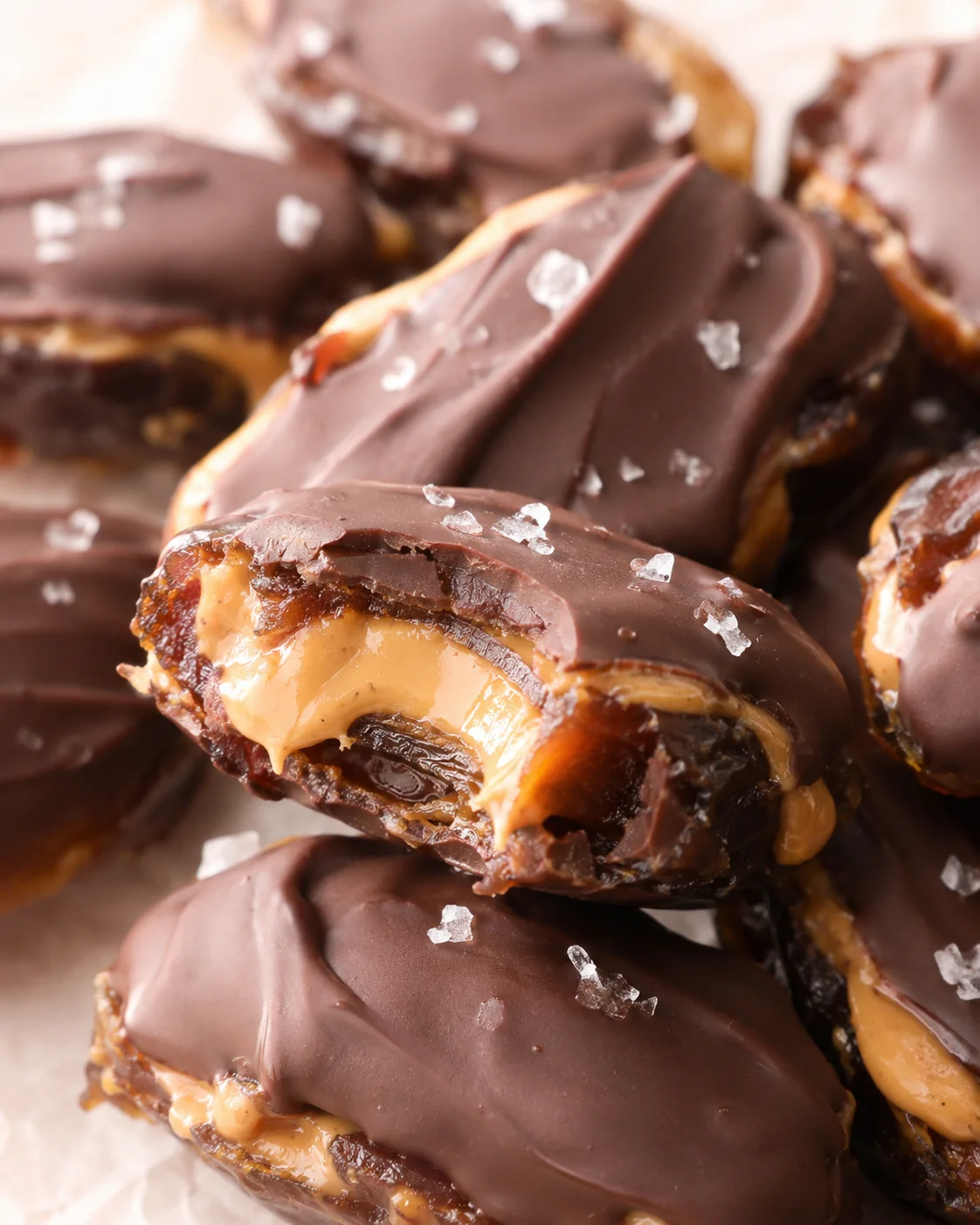 Close-up of glossy milk chocolate-coated peanut butter bites with flaky salt on parchment
