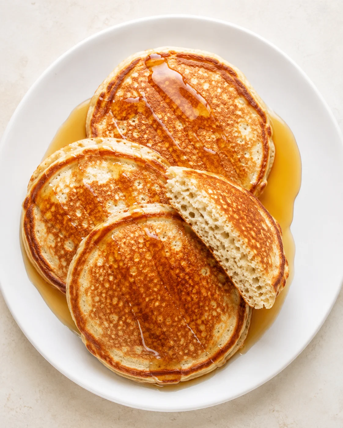 top-down view of a stack of golden pancakes drizzled with syrup on a white plate