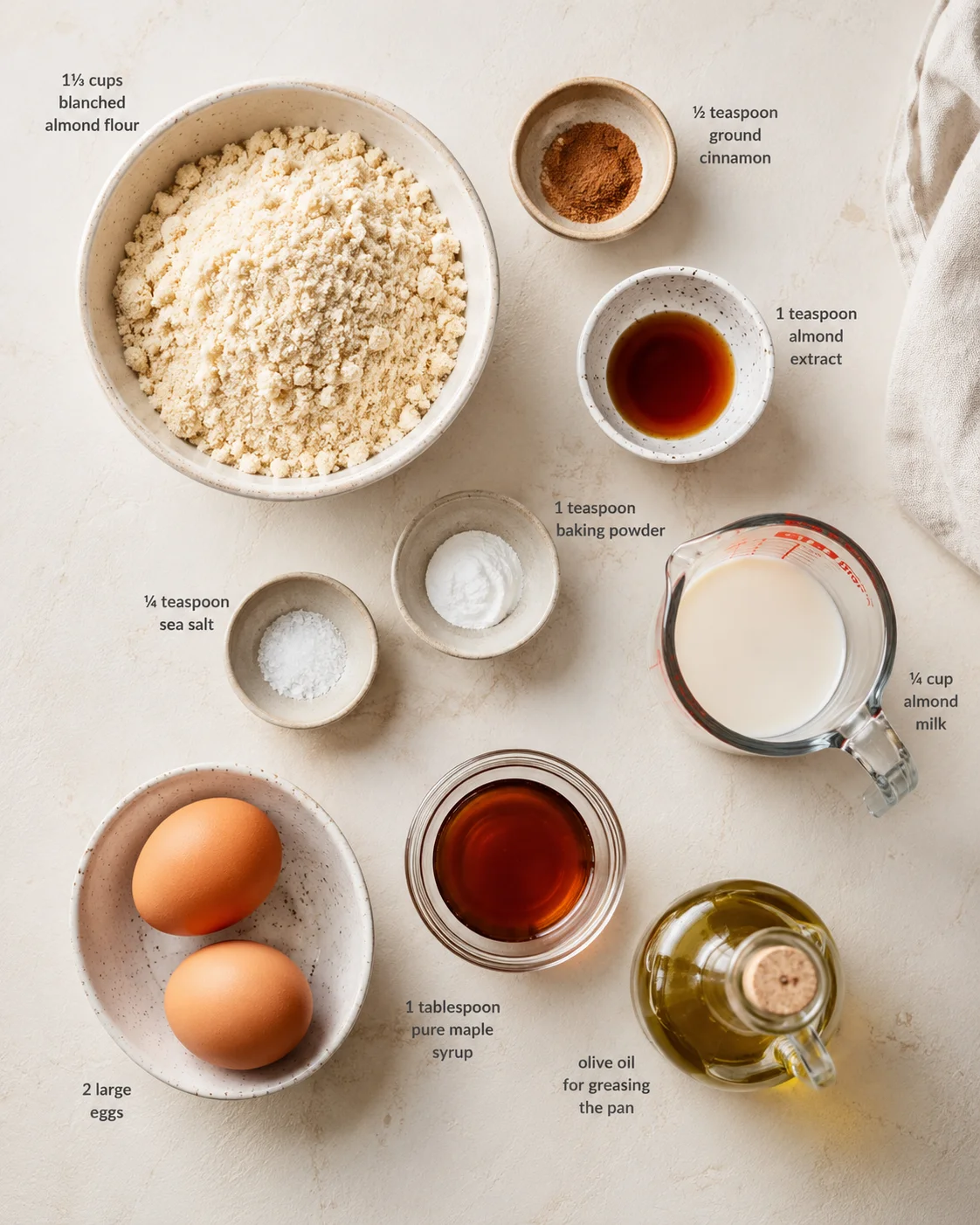 top-down view of almond flour, spices, eggs, milk, and oils arranged on a light kitchen surface