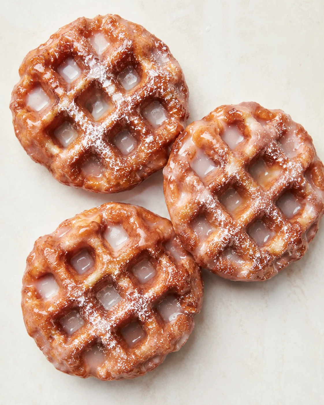 three round waffles with caramel glaze and powdered sugar on a light surface
