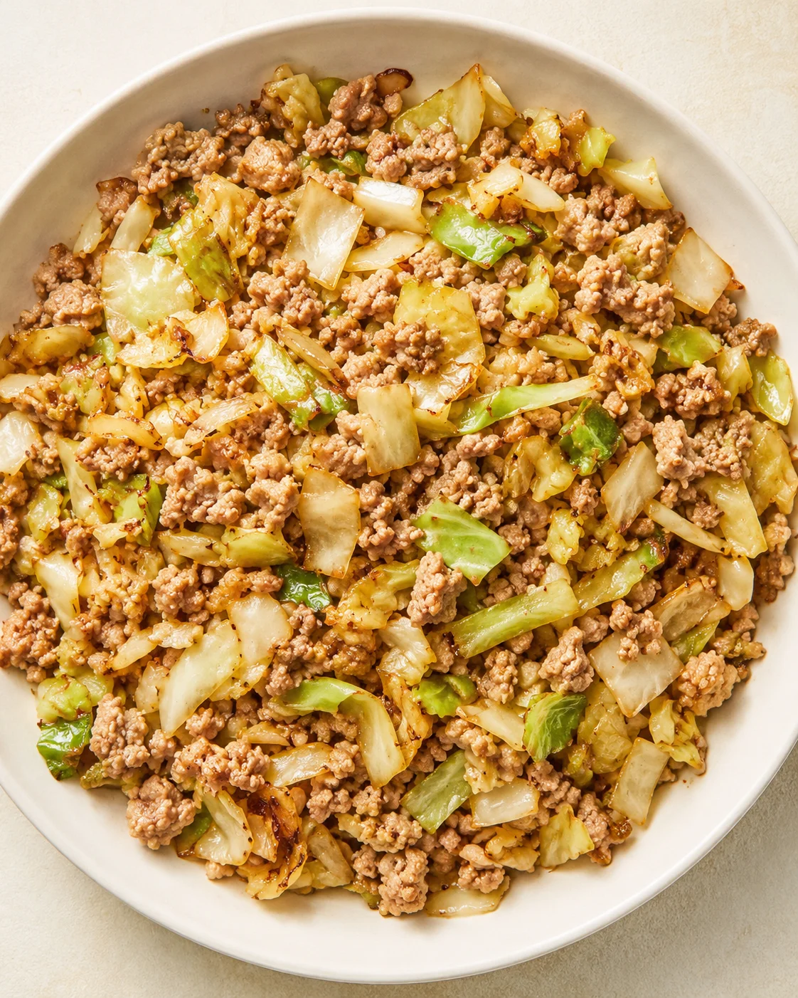 stir-fried ground pork with napa cabbage on a white plate, golden-brown edges