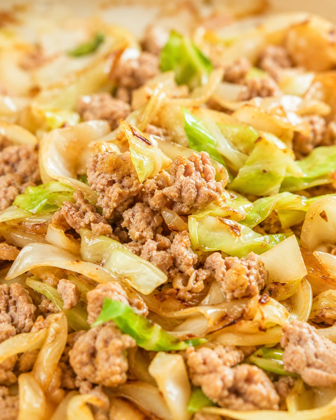 close-up of glossy pork and cabbage stir-fry with onions and browned edges