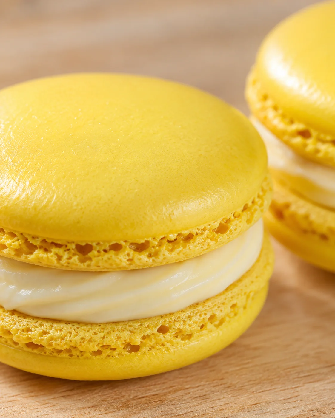 Close-up of bright yellow lemon macarons with white filling on a wooden board.