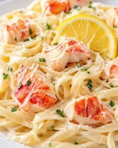 Creamy lobster pasta with lemon wedge, grated cheese, and parsley on a white plate.