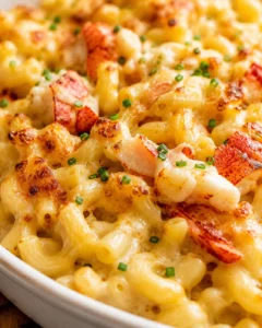 Creamy lobster macaroni and cheese with browned edges, tender pasta, and sprinkled green chives.