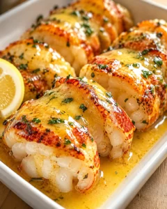 Lobster tails baked in a golden butter sauce with parsley, served in a white dish with a lemon wedge