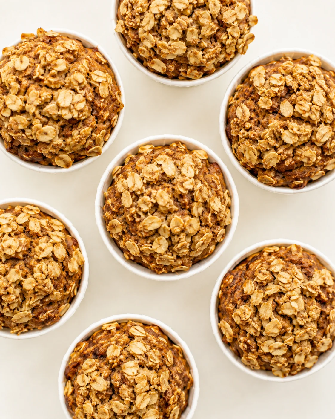 top-down view of several oat-topped muffins in white ramekins arranged on a pale background