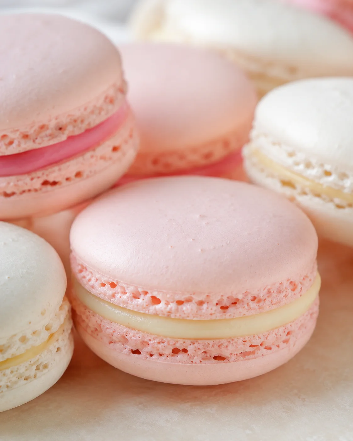 Close-up of pink and white macarons with creamy filling on a soft beige surface