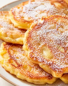 close-up of several golden fried dough discs dusted with powdered sugar on a plate
