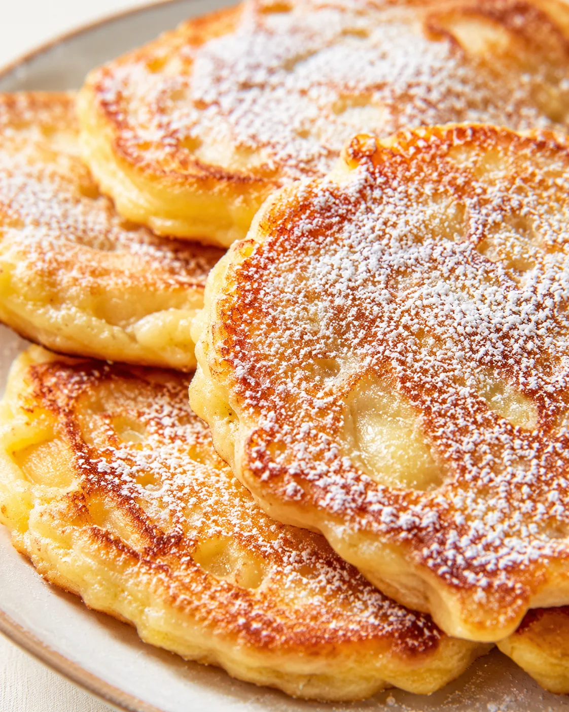 close-up of several golden fried dough discs dusted with powdered sugar on a plate
