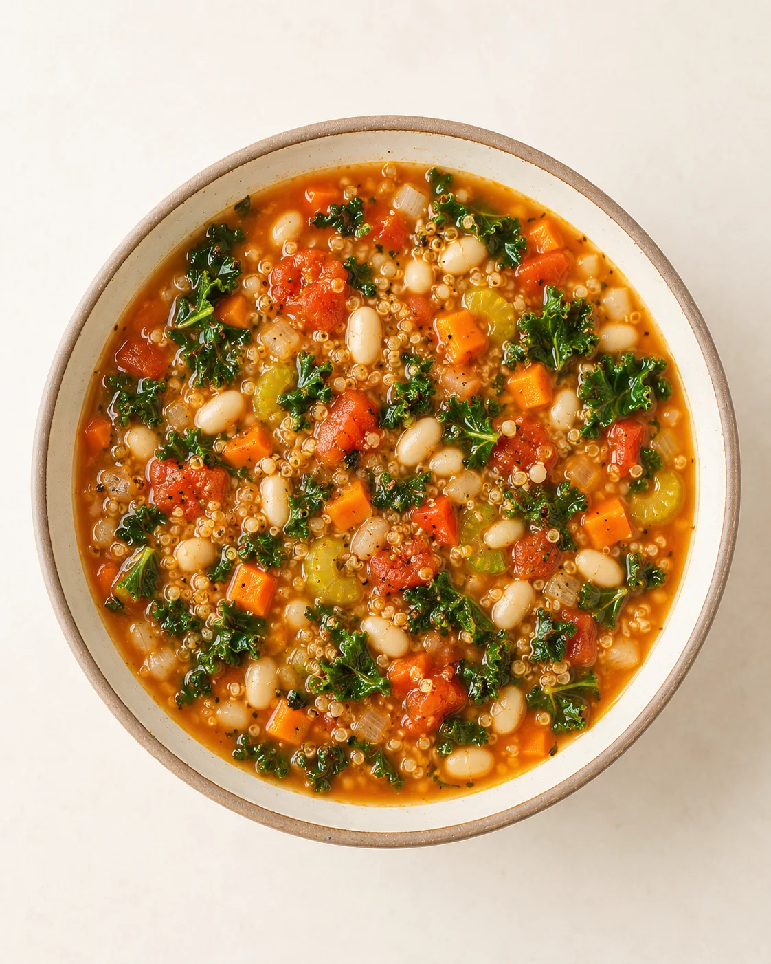 Top-down view of a bowl of tomato-based quinoa kale soup with white beans and diced vegetables
