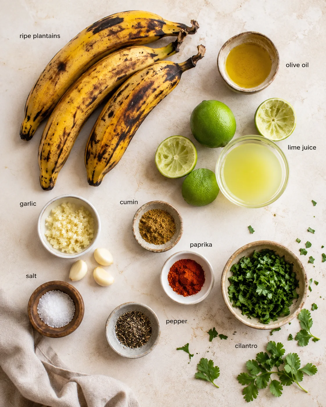 Overhead arrangement of ripe plantains, limes, garlic, spices, and cilantro on a beige countertop