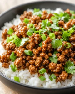 Close-up of glossy braised ground meat over white rice, garnished with green onions and cilantro.