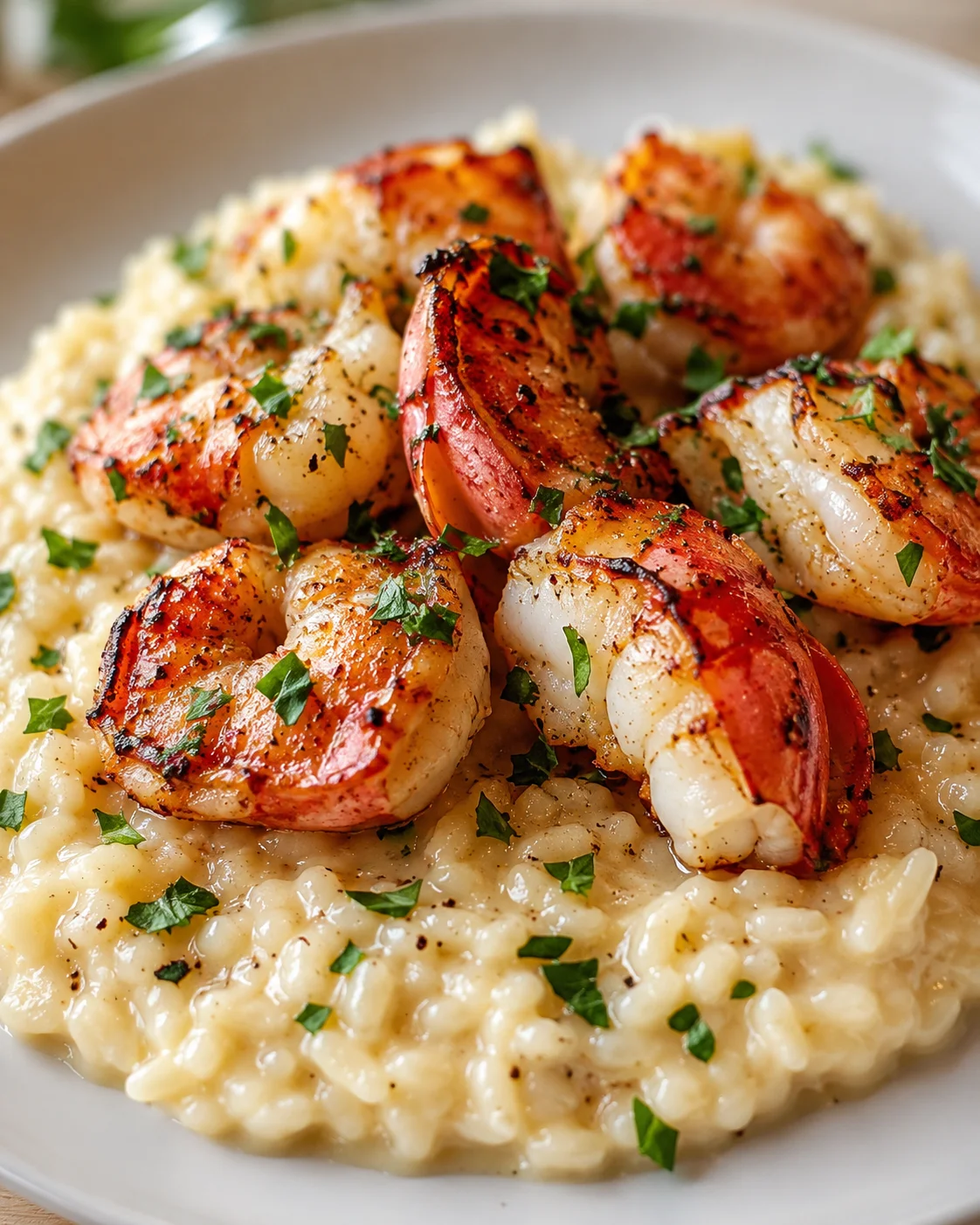plump grilled shrimp atop creamy risotto with chopped parsley on a white plate
