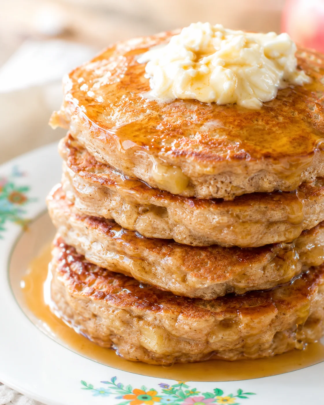 Tall stack of golden pancakes with melted butter and syrup on a floral-patterned plate.