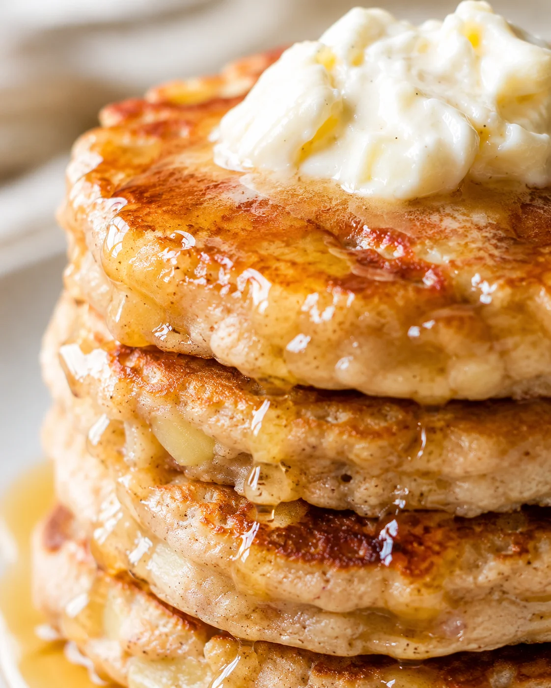 Close-up of a tall stack of golden pancakes with maple syrup and a scoop of butter on top.