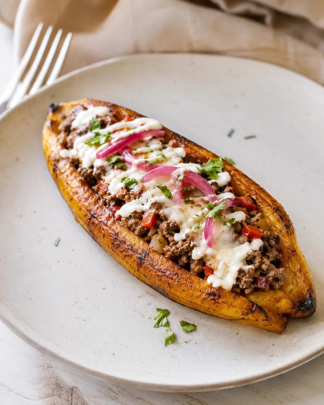 Half baked potato topped with beef, cheese, onions, and herbs on a beige plate.