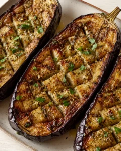 Baked eggplants seasoned with garlic, oregano, and lemon juice, garnished with fresh herbs.