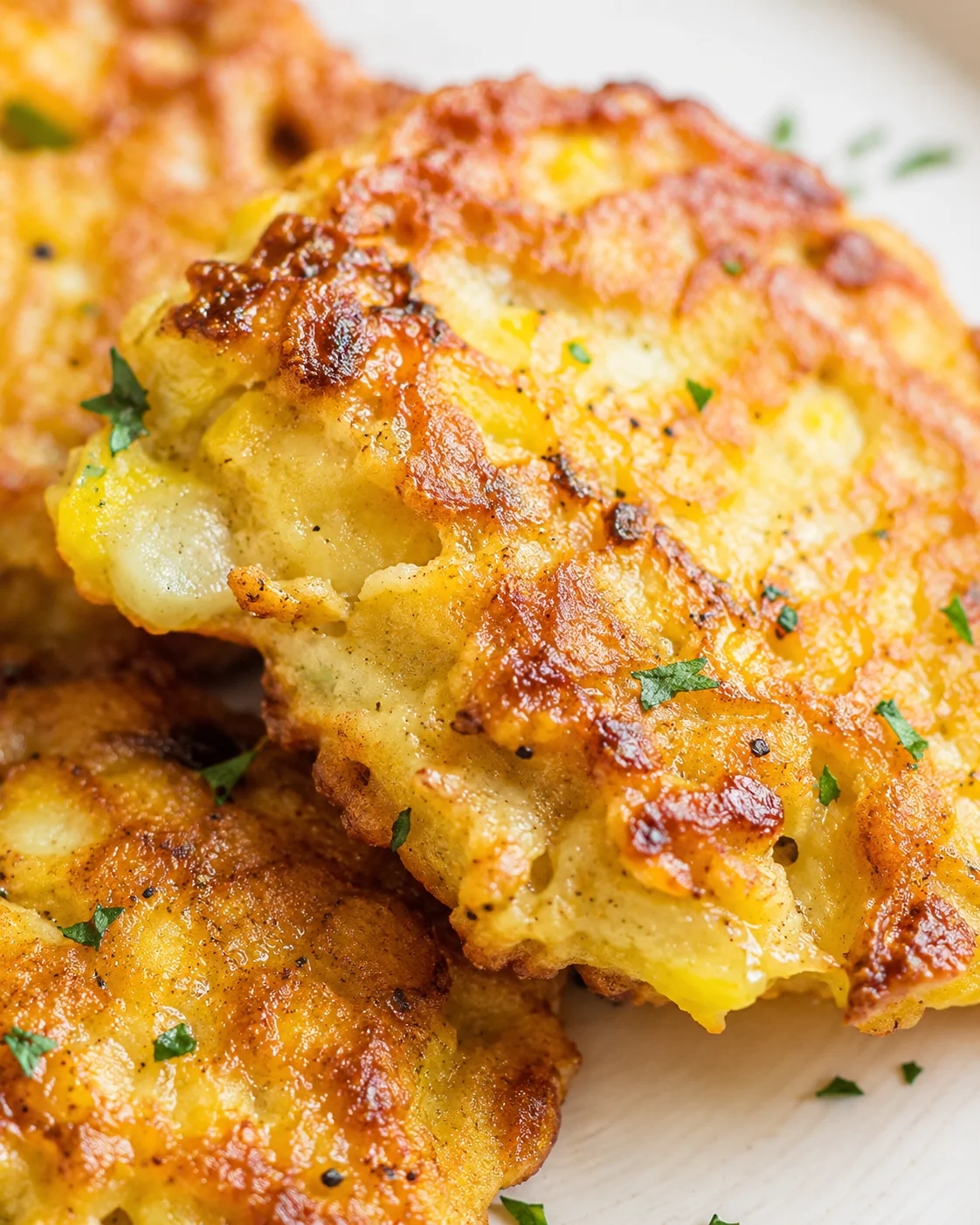 close-up of golden-brown cheesy potato fritters with parsley on a wooden board