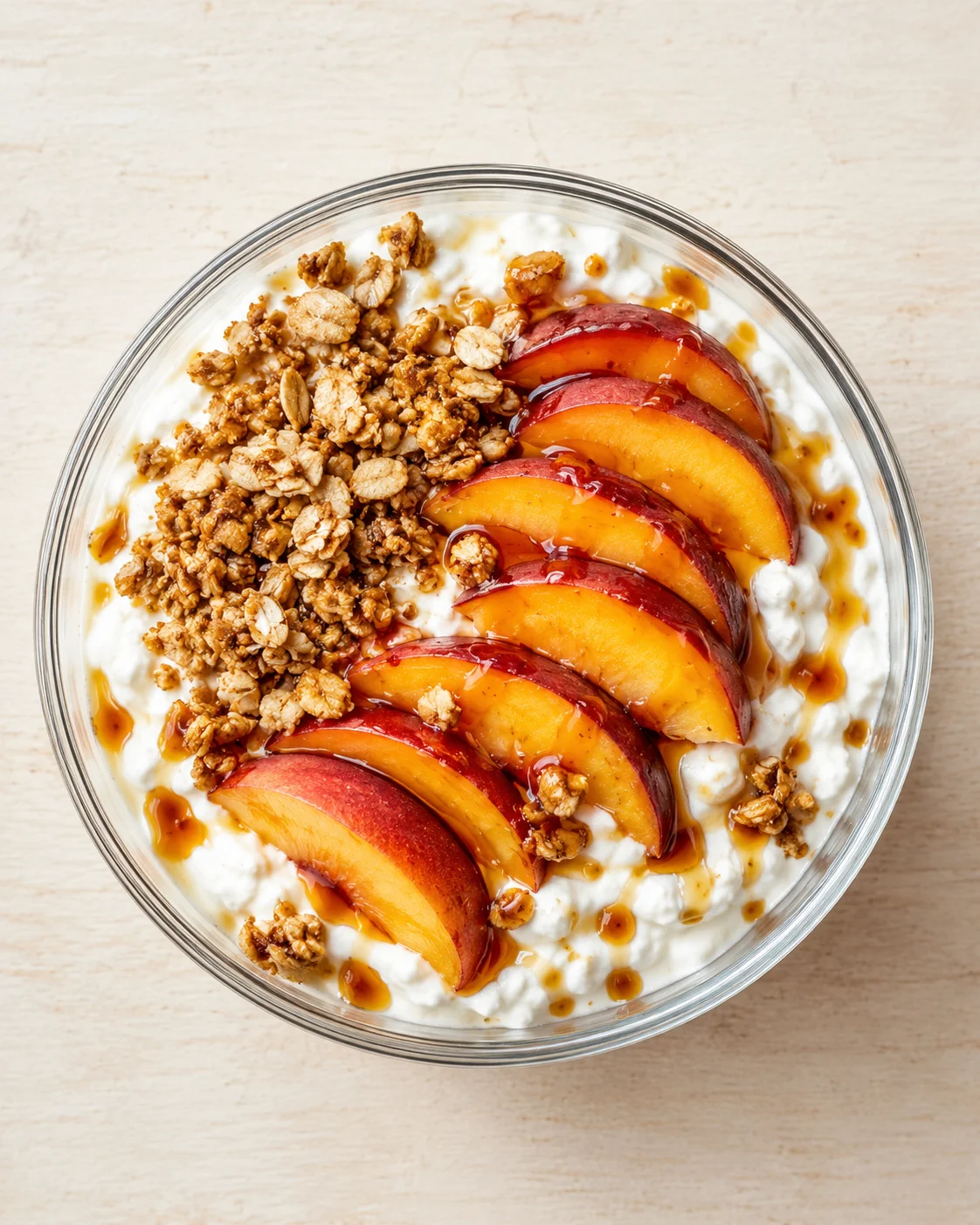 Top-down view of a yogurt bowl topped with granola, sliced peaches, and a caramel drizzle.
