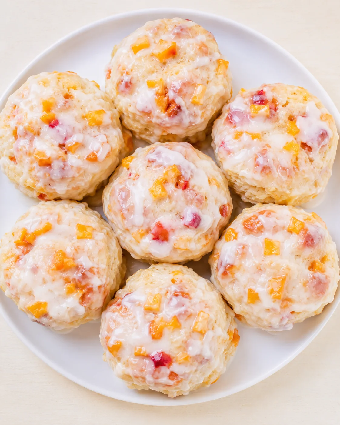 Plate of round, glazed scones studded with diced mango and peach on a white plate.