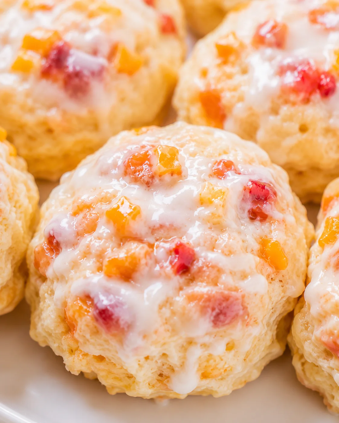 Peach Buttermilk Biscuits Close-up of warm, flaky peach biscuits with vanilla glaze and fruit chunks