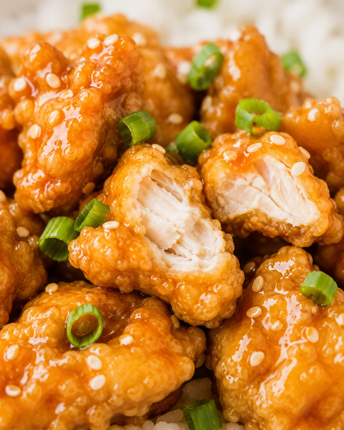 Crispy gluten-free orange chicken with a glossy, tangy orange sauce and green garnish