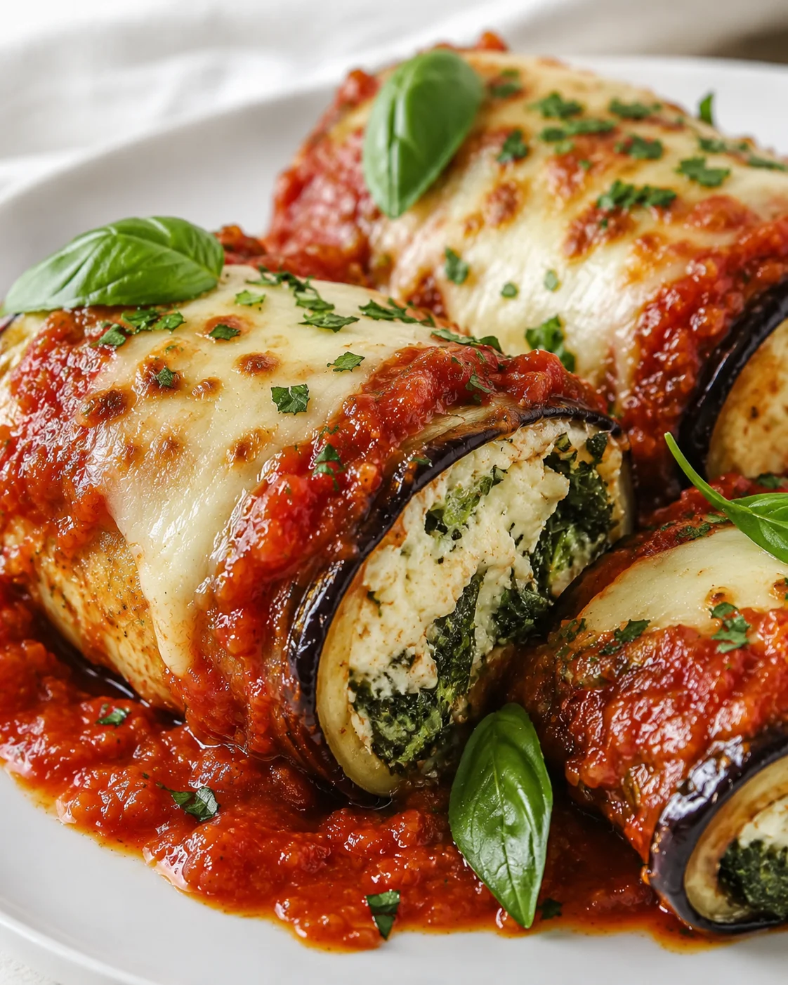 Delicious eggplant rollatini topped with melted cheese and fresh basil on a white plate