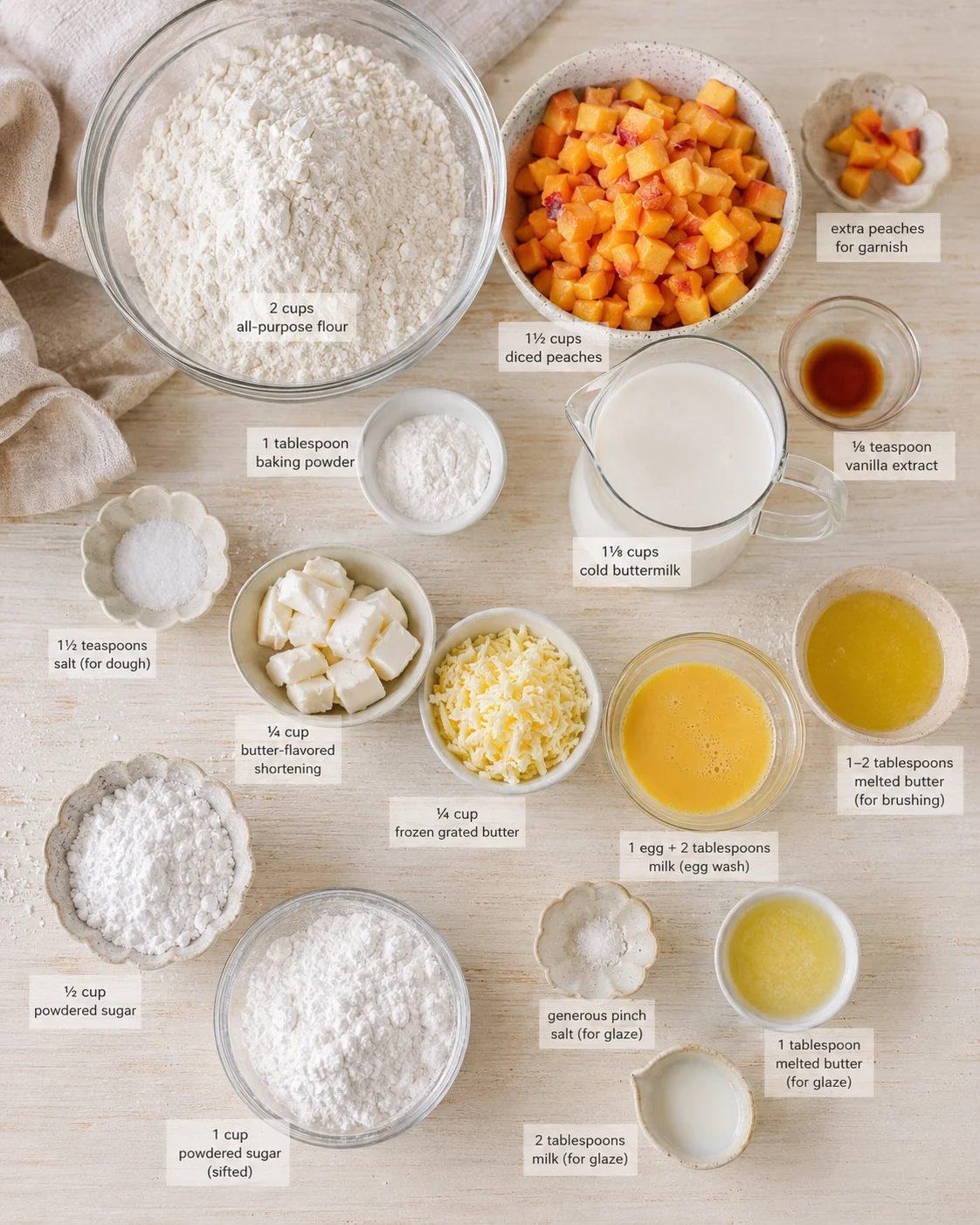 top-down view of labeled baking ingredients on a light wooden surface: flour, peaches, butter, milk