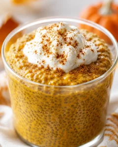 Close-up of a glass of pumpkin chia pudding topped with whipped cream and spices.