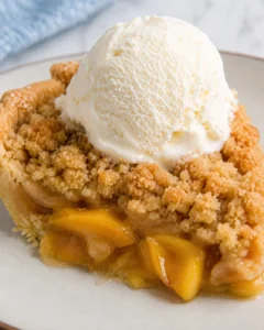 Close-up of peach crumble pie topped with a scoop of vanilla ice cream.