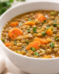 A bowl of warm carrot and lentil soup garnished with herbs and pepper.